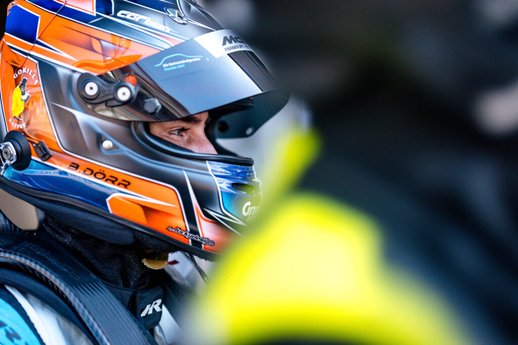 Rennfahrer Ben Dörr blickt mit einem orange-blauen Helm im Profil nach rechts.