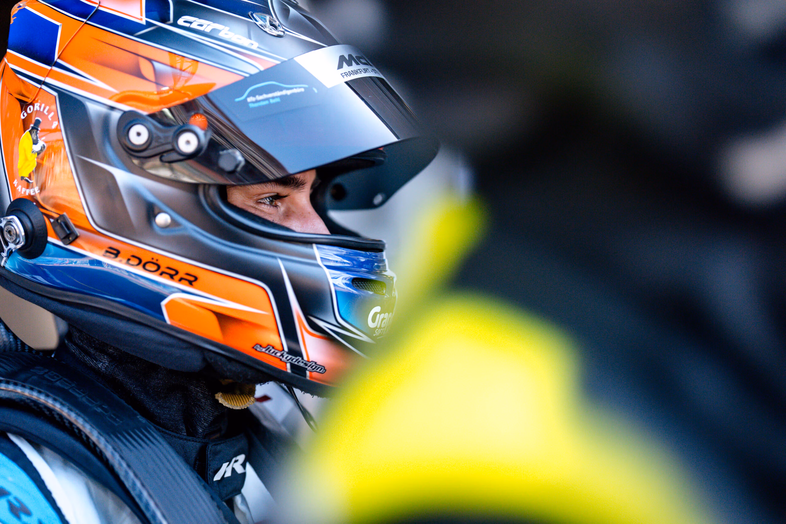 Rennfahrer Ben Dörr blickt mit einem orange-blauen Helm im Profil nach rechts.